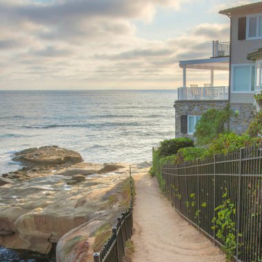Kaliforniya 'daki La Jolla' da suyun yakınındaki Kare Beyaz Kabarık Bulutlar. Demiryolu ve soldaki Pasifik Okyanusu manzaralı ve sağdaki sahil evi günbatımı gökyüzüne karşı..