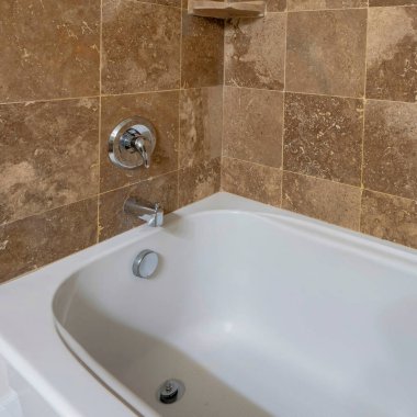 Duş başlığı ve musluğu duvara monte edilmiş kare bir küvet. Kahverengi karoları olan bir küvete yakın çekim ve sol köşedeki küçük raf..