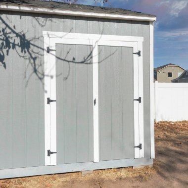 Gün batımında kare kabarık bulutlar. Gri metal. Evin arka bahçesinde çift kapılı döşeme var. Yapraksız bir ağacın altında, yanında aletler ve beyaz bir vinil çit olan bir alet kulübesi..