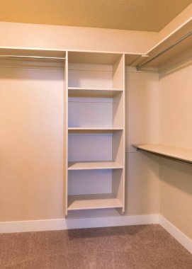 Sıcak renkli ışıklandırma ve raf üniteleri olan dikey boş bir dolap. Duvardaki rafların altında metal çubuklar ve ortada dikey çerçeve rafları olan penceresiz bir dolap..