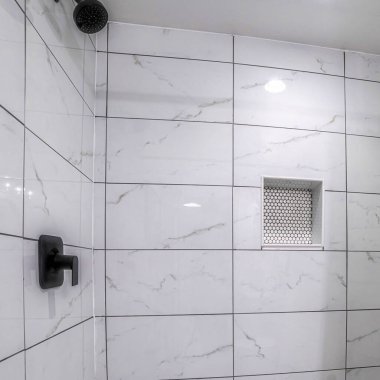 Mozaik döşemeli kare duş tezgahı ve siyah harçlıkla çevrili mermer fayanslar. Sol tarafta bir duş perdesi ve sağ tarafta da duvara monte edilmiş siyah duş başlığı var..