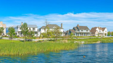 Panorama Fısıldayan Beyaz Bulutlar Oquirrh Gölü. Utah, Daybreak 'te bir yerleşim alanının ortasında. Gölün kıyısında asfalt bir yol var ve arka planda renkli evler var..