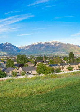 Dikey Whispy beyaz bulutları, Utah, Daybreak 'te dağ sıralı bir yerleşim bölgesinin panoramik görüntüsü. Çitlerle çevrili yerleşim alanının yakınında büyük bir çim tarlası var..