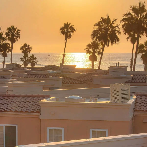 Square Roof decks with a view of the beach and palm trees at Oceanside, California. Roof decks of a mediterranean style accommodation buildings with red concrete tile roofs.