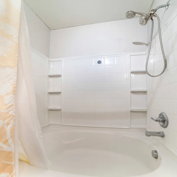 Square Bathtub and shower kit with corner shelves and two shower curtains. Bathroom interior with shower tub combo kit with wall mounted faucets and dual shower heads.