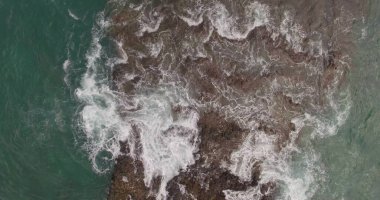 Büyük bir adanın kıyısındaki kayaların ve fırtınalı dalgaların resimli görüntüsü. Hava atışı