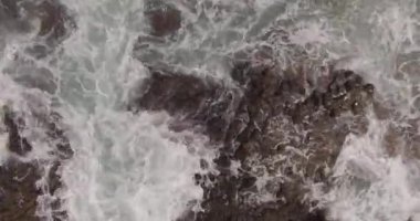 Büyük bir adanın kıyısındaki kayaların ve fırtınalı dalgaların resimli görüntüsü. Hava atışı
