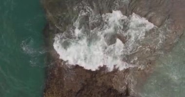 Büyük bir adanın kıyısındaki kayaların ve fırtınalı dalgaların resimli görüntüsü. Hava atışı
