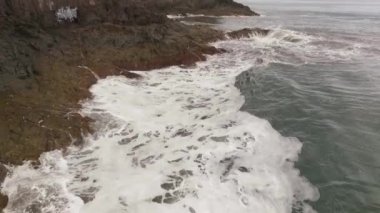 Kayalık bir sahil boyunca okyanus dalgaları. Yavaş çekim deniz manzarası, destansı kayalar ve dalgalar köye çarpıyor. Manzaranın sinematik drone görüntüsü