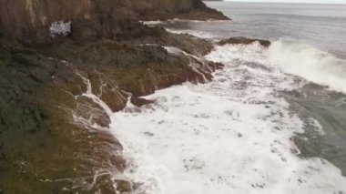 Kayalık bir sahil boyunca okyanus dalgaları. Yavaş çekim deniz manzarası, destansı kayalar ve dalgalar köye çarpıyor. Manzaranın sinematik drone görüntüsü
