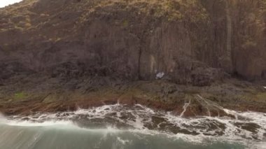 Kayalık bir sahil boyunca okyanus dalgaları. Yavaş çekim deniz manzarası, destansı kayalar ve dalgalar köye çarpıyor. Manzaranın sinematik drone görüntüsü