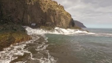 Kayalık bir sahil boyunca okyanus dalgaları. Yavaş çekim deniz manzarası, destansı kayalar ve dalgalar köye çarpıyor. Manzaranın sinematik drone görüntüsü