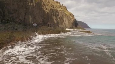 Kayalık bir sahil boyunca okyanus dalgaları. Yavaş çekim deniz manzarası, destansı kayalar ve dalgalar köye çarpıyor. Manzaranın sinematik drone görüntüsü
