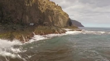 Kayalık bir sahil boyunca okyanus dalgaları. Yavaş çekim deniz manzarası, destansı kayalar ve dalgalar köye çarpıyor. Manzaranın sinematik drone görüntüsü