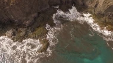 Kayalık bir sahil boyunca okyanus dalgaları. Yavaş çekim deniz manzarası, destansı kayalar ve dalgalar köye çarpıyor. Manzaranın sinematik drone görüntüsü