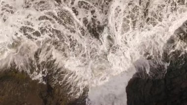 Kayalık bir sahil boyunca okyanus dalgaları. Yavaş çekim deniz manzarası, destansı kayalar ve dalgalar köye çarpıyor. Manzaranın sinematik drone görüntüsü