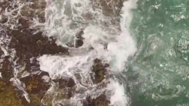 Kayalık bir sahil boyunca okyanus dalgaları. Yavaş çekim deniz manzarası, destansı kayalar ve dalgalar köye çarpıyor. Manzaranın sinematik drone görüntüsü