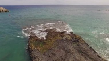 Kayalık bir sahil boyunca okyanus dalgaları. Yavaş çekim deniz manzarası, destansı kayalar ve dalgalar köye çarpıyor. Manzaranın sinematik drone görüntüsü