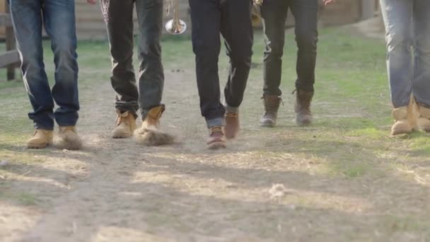 Nogi Kilku Mężczyzn Dżinsach Brązowych Butach Chodzących Brudnej Drodze Kopiących — Wideo stockowe