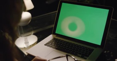 Akşam bir odada çalışan bir iş kadınının omzunun üstünden yeşil ekrana bakan bir bilgisayarın ışıkları kapalı bir şekilde. Yeşil laptop ekranlı dizüstü bilgisayar kullanılıyor.