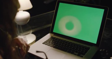 Akşam bir odada çalışan bir iş kadınının omzunun üstünden yeşil ekrana bakan bir bilgisayarın ışıkları kapalı bir şekilde. Yeşil laptop ekranlı dizüstü bilgisayar kullanılıyor.