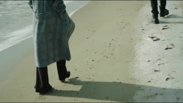 砂浜を歩くのは レインコートを着た女性と男とハイヒールのブーツ 脚を閉じて — ストック動画