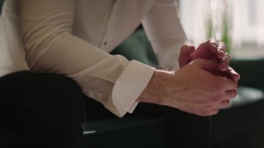 Kolları kıvrılmış beyaz gömlekli bir adam oturuyor. Eller ön planda. Renk düzeltmesi olmayan çekim, film kalitesi. Yüz tanıma olmadan yakın plan.