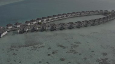 Sudaki bir bungalov villasının havadan görünüşü. Tropik Maldivler 'deki egzotik bir turkuaz cennetinin insansız hava aracı görüntüleri. Yüksek kaliteli 4K video. Maldivler 'de lüks bir tatil köyü. Renk düzeltmesi olmayan görüntü.