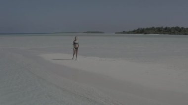 Egzotik tropik Maldivler 'in kumlu sahilinde atlayan neşeli kız. Gülümseyen neşeli bayan sahilde eğleniyor, güneşin ve berrak suyun tadını çıkarıyor. Renk düzeltmesi olmayan görüntü.