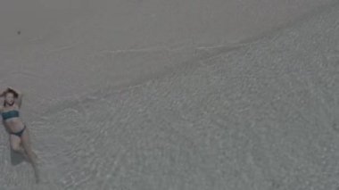 Sahilde yatan ve denizin dalgalarıyla yıkanan bir kızın en güzel görüntüsü. Kesinlikle temiz ve şeffaf su. Tropikal plajın havadan görünüşü, beyaz kumsal manzarası. Renk düzeltmesi olmayan görüntü.