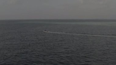 Açık bir yaz gününde arka planda küçük bir adayla birlikte Maldivler 'deki Hint Okyanusu' nda yavaşça ilerleyen küçük beyaz bir teknenin hava görüntüsü. Renk düzeltmesi olmayan görüntü.