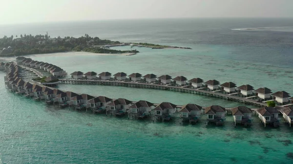 Mavi göldeki, beyaz kumlu sahildeki lüks villaların havadan görünüşü. Maldivler 'de sıralanmış su üzerinde bungalovları olan bir ada..