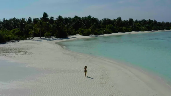 Egzotik tropik Maldivler 'in kumlu sahilinde atlayan neşeli kız. Gülümseyen neşeli bayan sahilde eğleniyor, güneşin ve berrak suyun tadını çıkarıyor..