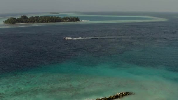 在一个晴朗的夏日 空中拍摄到一艘白色小船缓缓驶过印度洋 在马尔代夫的一个偏远小岛的背景下航行 — 图库视频影像
