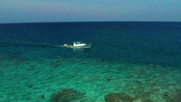 在一个晴朗的夏日 空中拍摄到一艘白色小船缓缓驶过印度洋 在马尔代夫的一个偏远小岛的背景下航行 — 图库视频影像