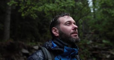 Bir erkek turistin portresi, sokakta sağanak yağmurun altında duruyor ve ıslanıyor, kenarlara bakıyor. Yavaş çekim.