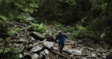 Sırt çantalı ve mavi ceketli yalnız bir gezgin yağmurlu havada ormanda kayalık arazide yürüyor. Dağlara tek başına gitme fikri..