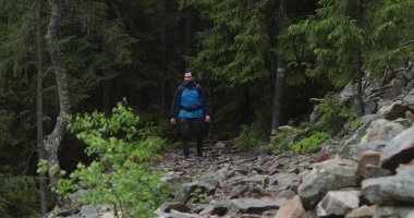 Formda bir genç adam kayalık bir arazide tek başına yürüyor, ormandan çıkıyor. Yalnız seyahat eden bir adam konsepti..