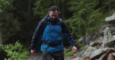 Formda bir genç adam kayalık bir arazide tek başına yürüyor, ormandan çıkıyor. Yalnız seyahat eden bir adam konsepti..