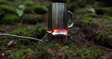 Metal bardak, bir gezginin tatili sırasında ormanda gaz ocağında ısıtılır. Tek başına çay yapma kavramı..