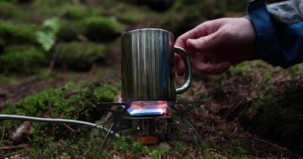 旅行者の休暇中 屋外の森のガスバーナーで金属製のマグカップが加熱されます 一人旅でお茶を作るというコンセプト — ストック動画