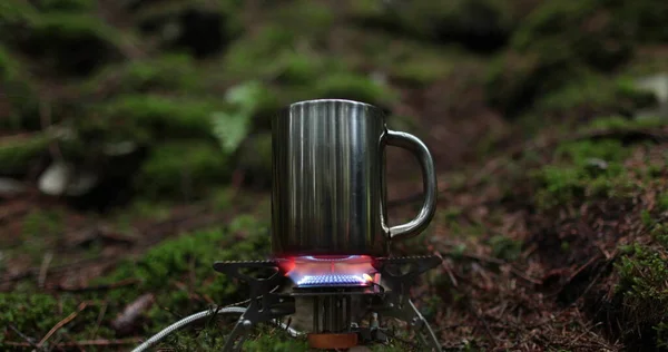 stock image A metal mug is heated on a gas burner in the forest outdoors during a traveler's vacation. The concept of making tea in solo travels.