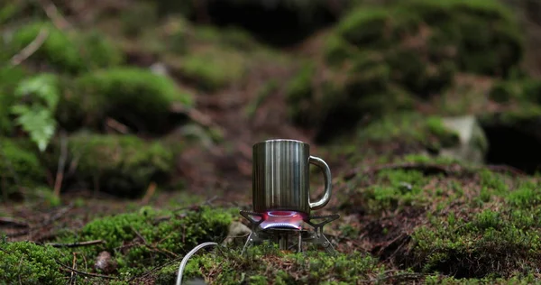 Metal bardak, bir gezginin tatili sırasında ormanda gaz ocağında ısıtılır. Tek başına çay yapma kavramı..