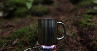 Metal bardak, bir gezginin tatili sırasında ormanda gaz ocağında ısıtılır. Tek başına çay yapma kavramı..