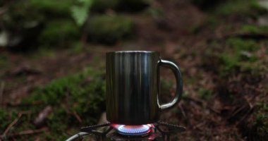 Metal bardak, bir gezginin tatili sırasında ormanda gaz ocağında ısıtılır. Tek başına çay yapma kavramı..