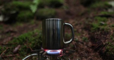 Metal bardak, bir gezginin tatili sırasında ormanda gaz ocağında ısıtılır. Tek başına çay yapma kavramı..