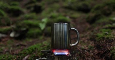 Metal bardak, bir gezginin tatili sırasında ormanda gaz ocağında ısıtılır. Tek başına çay yapma kavramı..