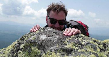 Bir erkek tırmanıcı elinden gelenin en iyisini yaparak zirveye ulaşır. Kayanın yüksekliğinin üstesinden gelme anı. Dağdan dağcıya görüntüyü göster.