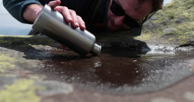 Susamış ve zinde bir turist sert dağ koşullarında küçük bir su birikintisinden su içiyor. Dağ yaşamı konsepti. Kayalık dağlarda zor şartlarda bir turist.