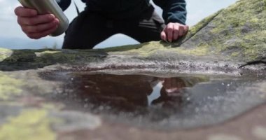 Susamış ve zinde bir turist sert dağ koşullarında küçük bir su birikintisinden su içiyor. Dağ yaşamı konsepti. Kayalık dağlarda zor şartlarda bir turist.